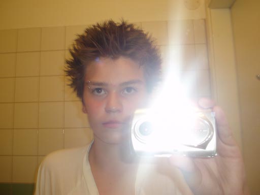 Ossi is taking a picture with flash in the mirror, his hair is fluffy, he is looking into the camera
